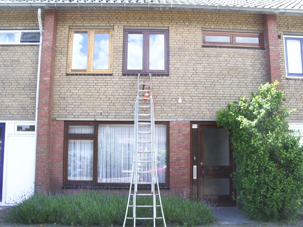 Dezelfde gevel voor het schilderwerk, met de ladder tegen de gevel en een kozijn nog in de grondverf