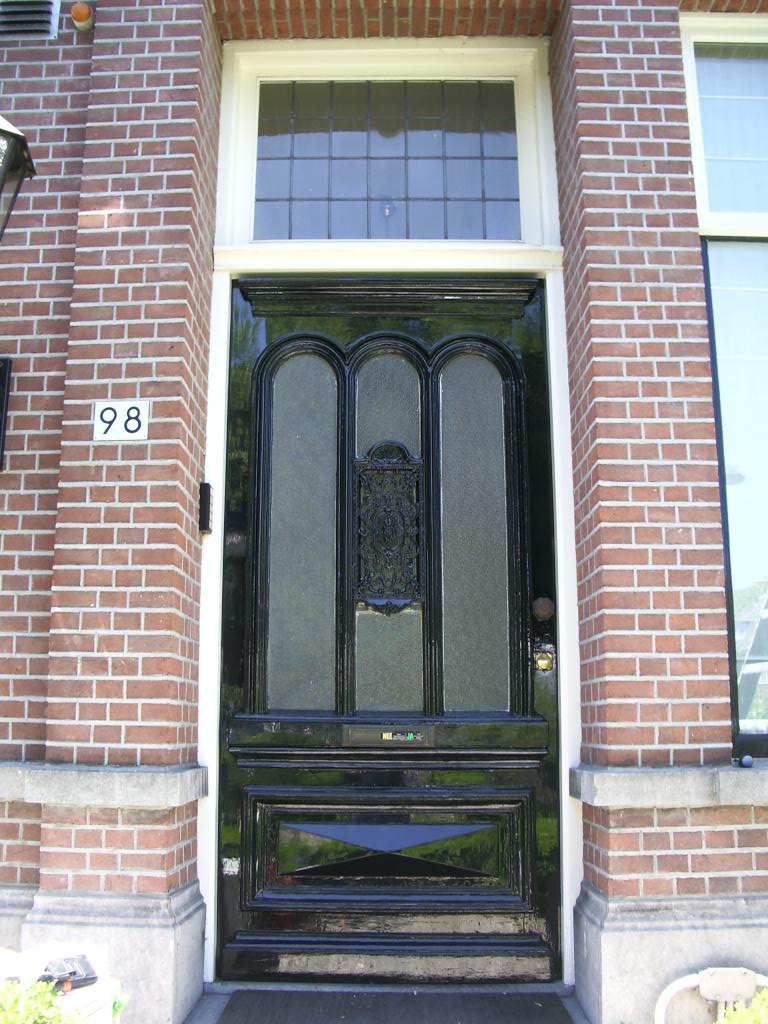 Hoogglans zwart geschilderde voordeur met glas in lood bovenlicht in een bakstenen gevel