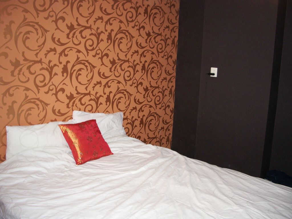 Slaapkamer met koperkleurig behang met ornamenten en een donkere wand